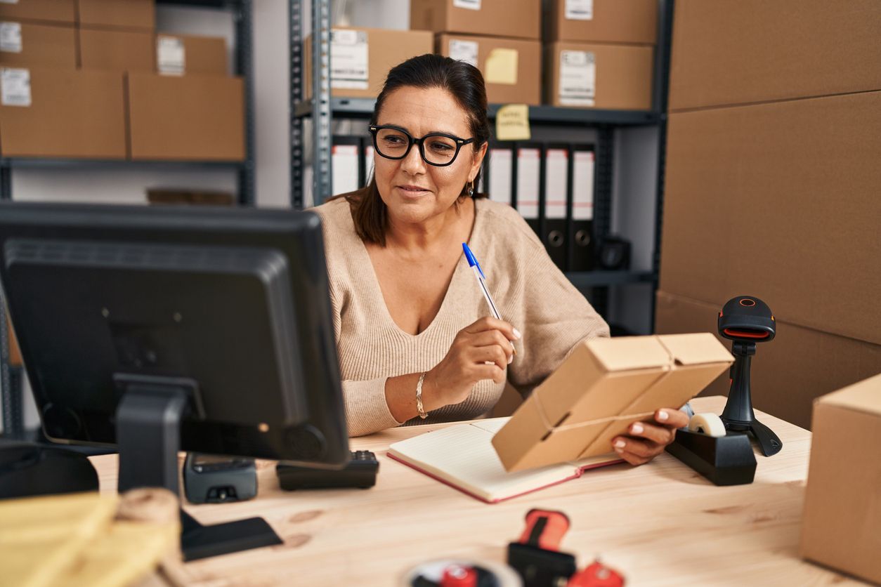 Small business employee in a warehouse with boxes and computer.